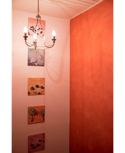 Flur mit Kronleuchter, oranger Wand und vier quadratischen Bildern in verschiedenen Farben.