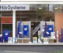 Schaufenster eines Geschäfts für Hörsysteme mit blauen Dekorationen und verschiedenen Produkten.