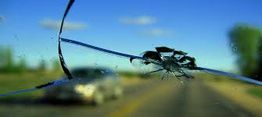 Cracked car windshield with a blurred road and sky in the background.