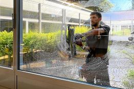 Mann putzt Glasfenster von außen, Hintergrund mit Gartenansicht.