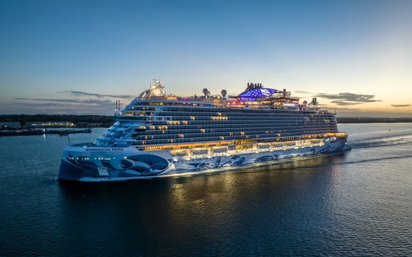 Ein beleuchtetes Kreuzfahrtschiff fährt bei Dämmerung in einen Hafen ein.