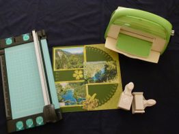 Scrapbooking-Ausrüstung: Papierschneider, Stanzgerät, Fotos und Verzierungen auf dunklem Hintergrund.