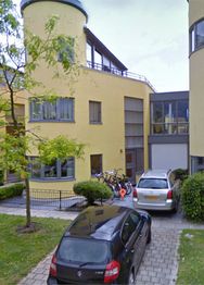 Geel gebouw met ronde torens, fietsen en auto's op de oprit.