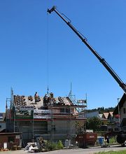 Kran hebt Baumaterial auf ein Gerüst eines im Bau befindlichen Hauses bei blauem Himmel.