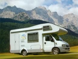 Weißes Wohnmobil vor einer Berglandschaft, unter blauem Himmel geparkt.