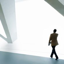 Person walking in a modern, minimalist building with large geometric structures.