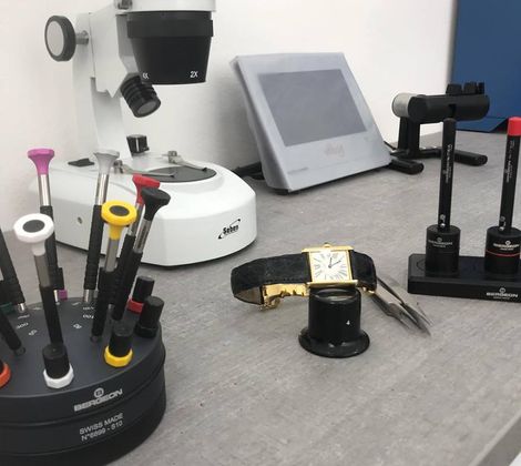 Banco con strumenti per la riparazione di orologi, inclusi cacciaviti e lente d'ingrandimento.