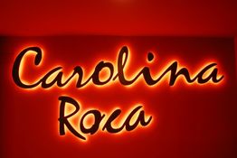 Texto iluminado dice "Carolina Roca" sobre fondo rojo.