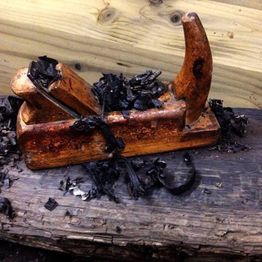 Cepillo de carpintero sobre madera quemada, rodeado de virutas y cenizas.