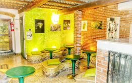 Locale con pareti in mattoni e tavoli verdi, decorato con quadri e cuscini colorati.