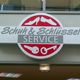 Schild mit Aufschrift "Schuh & Schlüssel Service" und Symbolen für Schuhe und Schlüssel.