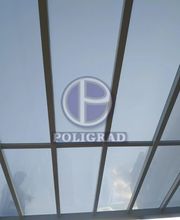 Cobertura de vidro com estrutura metálica e alguém refletido ao fundo. Logotipo Poligrad visível.