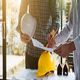 Two people reviewing construction plans with hard hats and small house models on the table.