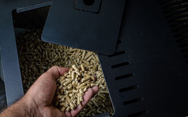 Eine Hand eines Mannes befüllt einen Pelletofen mit neuen Pellets.