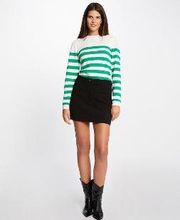 Mujer con suéter de rayas verdes y falda negra, posando con botas negras.