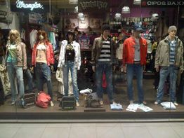 Schaufenster mit bekleideten Schaufensterpuppen in Freizeitkleidung, umgeben von Accessoires.