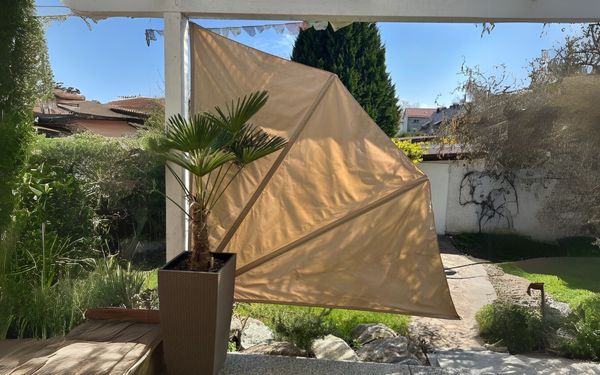 Beiger Balkonfächer auf sonniger und bepflanzter Terrasse.