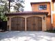 Stucco house with wooden double garage doors and a tiled roof, surrounded by trees.