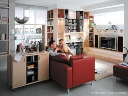 Paar entspannt auf rotem Sofa in modernem Wohnzimmer mit Bücherregalen und Fernseherwand.