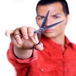 Man in red shirt holding scissors towards the camera.