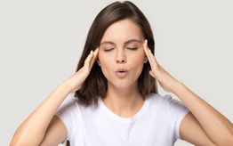 Donna con occhi chiusi, mani sulle tempie, in concentrazione o sollievo, su sfondo neutro.