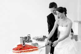 Brautpaar schneidet gemeinsam eine herzförmige Erdbeertorte an.