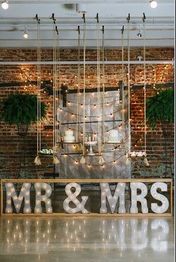 Industrial wedding decor with "MR & MRS" marquee lights, swings, and hanging greenery.