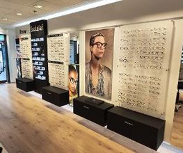 Optiekwinkel met brillen op display en grote foto's van gemodelleerde brillen aan de muur.
