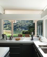 Cocina moderna con ventana grande, vista al jardín y colinas. Electrodomésticos sobre la encimera.