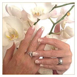 Hände mit Nageldesign und Ringen halten weiße Orchideen.