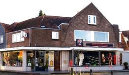 Bakstenen gebouw met winkel, etalages vol sportkleding en bokspoppen, en een groot raam boven.