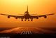 Aereo atterra su pista al tramonto, con cielo arancione intenso.