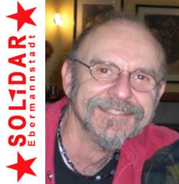 Älterer Mann mit Brille und Bart lächelt. Rotes Solidar Ebermannstadt-Logo an der Seite.