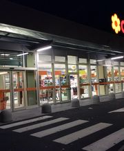 Ingresso di un supermercato Conad illuminato di notte, con strisce pedonali e carrelli visibili.