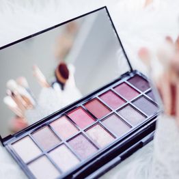 Eyeshadow palette with mirror, featuring pink and neutral shades, with brushes reflected.