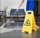 Person mopping floor near caution sign in a reception area, with chairs and plants visible.