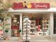 Kleiner Laden mit roten Vordach, Schaufenster voller Spielzeug und Regal mit Grußkarten außen.