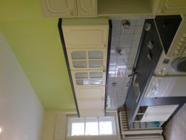 Weiße Küche mit grauer Arbeitsplatte, Spüle, Hängeschränken und grün gestrichenen Wänden.