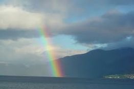 Arcobaleno sul mare con montagne e cielo nuvoloso.
