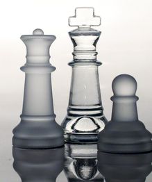 Drei Schachfiguren aus Glas auf einer reflektierenden Oberfläche.