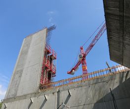 Baustelle mit großem Kran und halb errichtetem Betonbau gegen blauen Himmel.