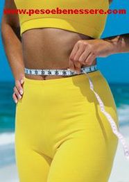 Donna in abbigliamento giallo misura la vita con un metro su una spiaggia.