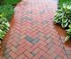 Brick pathway with herringbone pattern, bordered by green plants on both sides.