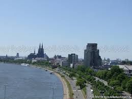 Rheinpanorama mit Dom und moderner Architektur, Bäume und Autos entlang der Uferstraße.