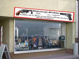 Außenseite eines Waffenladens mit Schaufenster voller Verkaufsartikel und Werbeschild darüber.