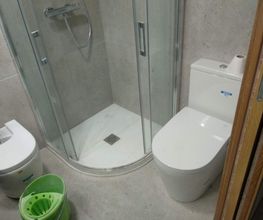 Baño moderno con ducha de cristal, inodoro, bidé y balde verde.