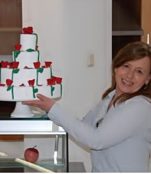 Frau präsentiert eine mehrstöckige Torte mit roten Rosen neben einer Glasvitrine.
