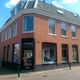 Rood bakstenen hoekpand met grote ramen en een kapperszaak op de begane grond.
