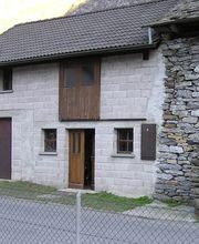 Steinhaus mit Holzelementen, zweistöckig, Zaun im Vordergrund, Berglandschaft im Hintergrund.