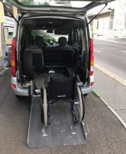 Rollstuhl auf einer Rampe im Kofferraum eines Autos neben einer Straße.